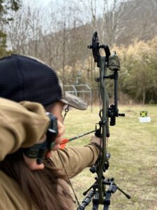 Woman holds bow aimed steadily at target before shooting.